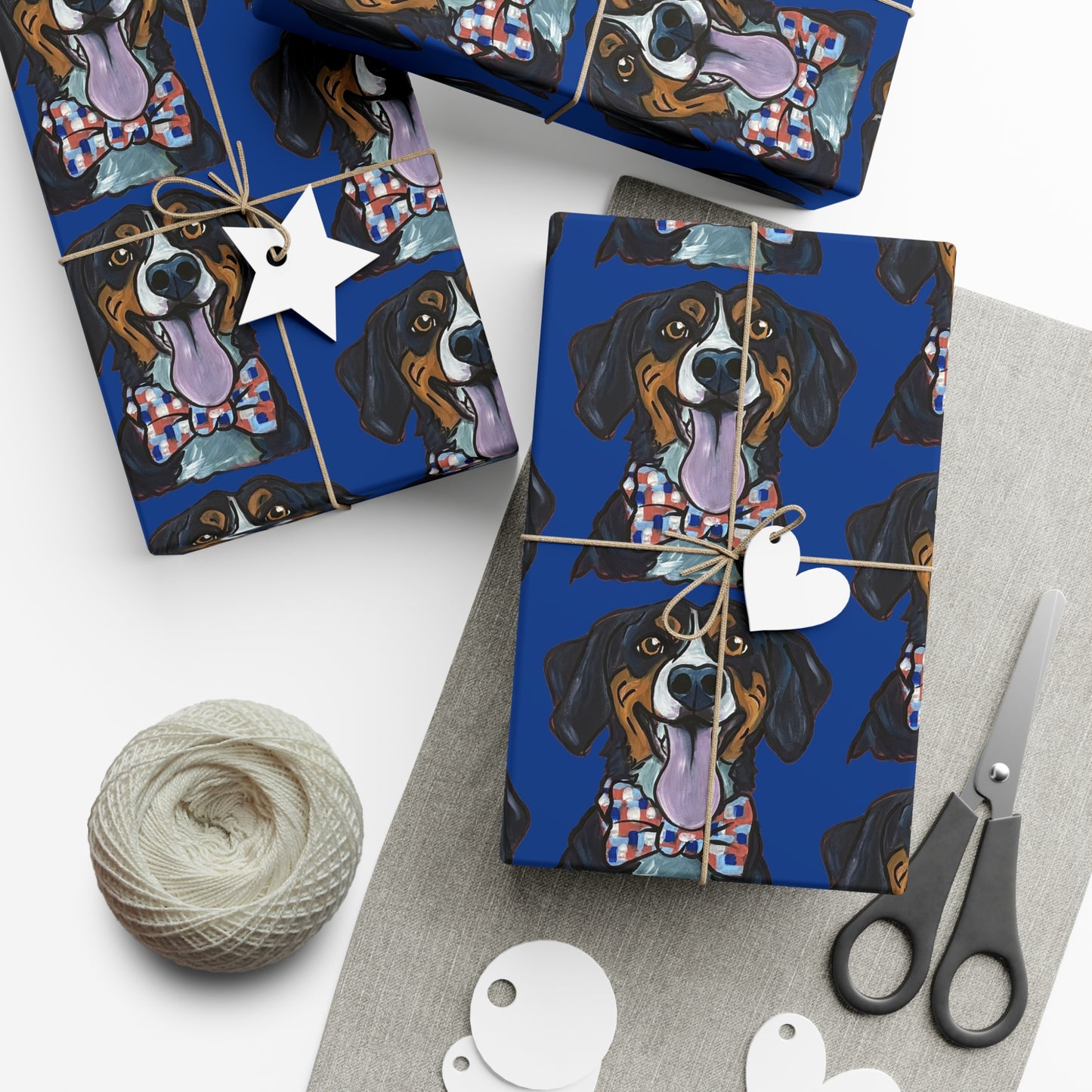 Gift wrap with dog pattern on blue background, scissors, yarn, and tags on white surface